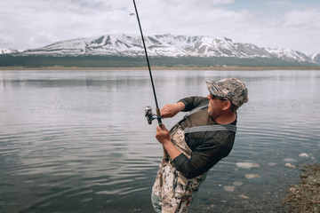 The guy fishing on the shore of a mountain lake . Reflection of mountains in water