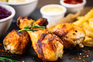 Grilled drumsticks with french fries and vegetables on wooden background