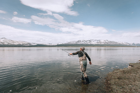 The guy fishing on the shore of a mountain lake . Reflection of mountains in water