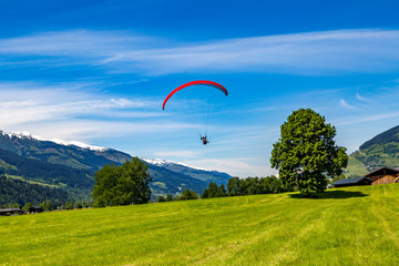 ein Gleitschirmflieger will auf einer Wiese landen, im Hintergrund Berge