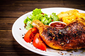 Roasted chicken leg with french fries and vegetable salad on wooden background