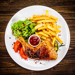Roasted chicken leg with french fries and vegetable salad on wooden background