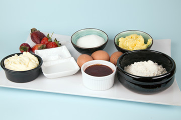 Ingredients for cooking strawberries mug cakes. Flour, butter, sugar, caramel in ceramic bowls, milk, strawberries and salt.