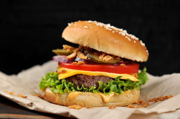 Cheeseburger on craft paper. Dried onions are scattered around the cheeseburger. Black background. Close-up. Macro shooting.