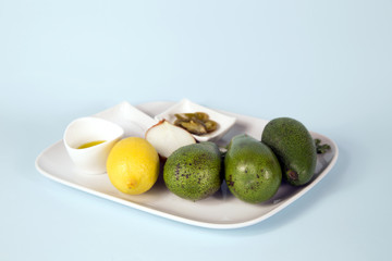 Ingredients for homemade guacamole: Avocado, Lemon, Salt and Pepper top view isolated blue background