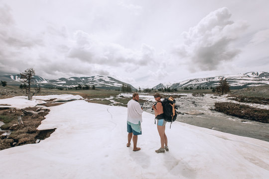 Naked Tourist In Shorts With A Backpack Goes To The Mountains. The Snow Around