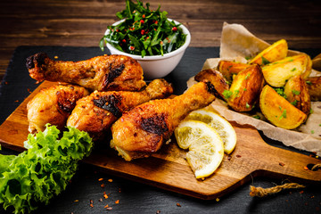 Grilled chicken drumsticks with baked potatoes and vegetable salad on wooden table