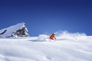 Skier skiing downhill in high mountains against blue sky