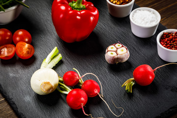 Ingredients for vegetable salad on black stone plate on wooden background