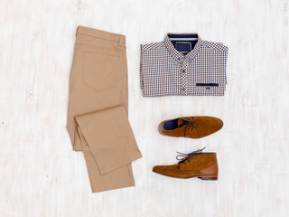 Beige pants, plaid shirt and brown suede shoes. Overhead view of men's casual outfit on white wooden background. Flat lay, top view.