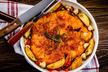 Fried pork chop, baked potatoes and vegetables in pan on wooden background