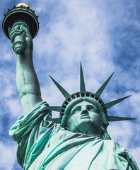 Fototapeta premium Estatua de la libertad, vista desde un ángulo bajo, con fondo nublado y cielo azul, en la Isla de la Libertad de Nueva York, EE. UU.,