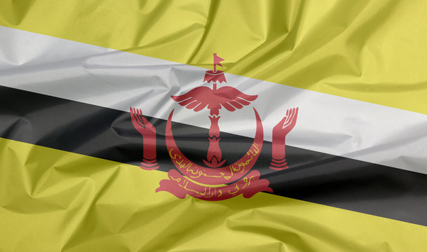 Fabric flag of Brunei Darussalam. Crease of Brunei flag background, red crest on yellow field cut by black and white diagonal stripes.
