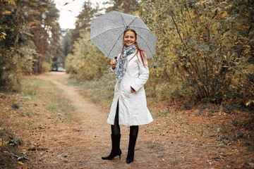 beautiful Caucasian middle-aged woman with red hair with an umbrella in the Park on a cloudy autumn day