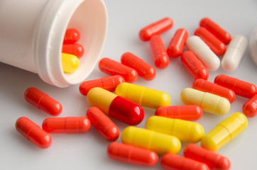 Red capsules pill spilled out of white plastic bottle. Global healthcare concept. Antibiotics drug resistance. Antimicrobial capsule pills. Pharmaceutical industry. Pharmacy.