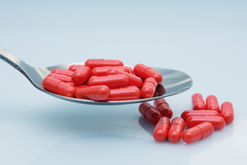 red capsules on a spoon, tablets scattered on a table