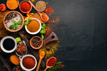 Spices and herbs on a wooden board. Pepper, salt, paprika, basil, turmeric. On a black wooden chalkboard. Top view. Free copy space. - obrazy, fototapety, plakaty