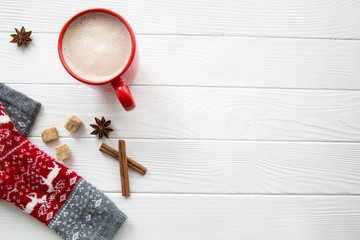 Red Christmas socks with deer and ornament on white wooden background. Hot chocolate in red cup with spices: anise stars, brown sugar and cinnamon rolls. Copy space.