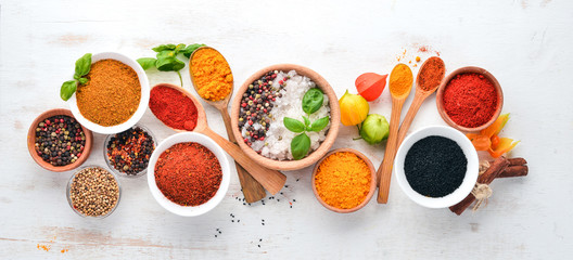 A set of Spices and herbs on a white wooden table. Basil, pepper, saffron, spices. Indian...