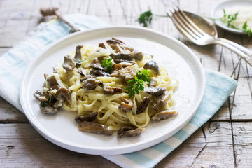Tagliatelle with cream and forest mushrooms sauce in a white plate on a wooden background. Rustic style.