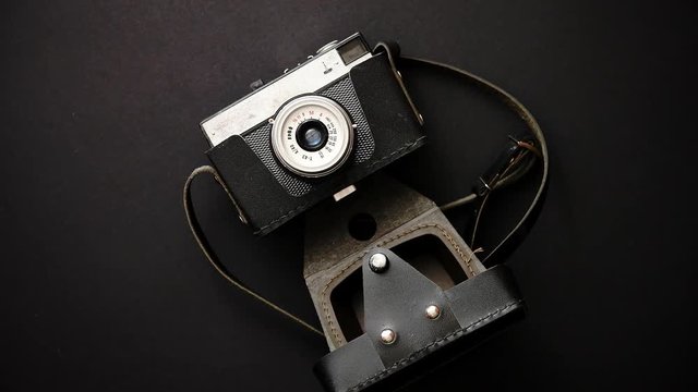 Old retro film camera in leather case on black background. Top view.