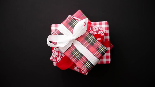 Stack of gifts boxes wrapped with red checkered pattern christmas paper with white bow on black table, top view