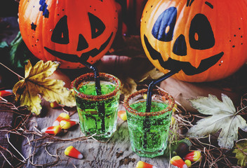 Halloween composition with festive green drink and smiling drinking pumpkins, with sweet corn, straw and fallen leaves on dark background, selective focus © 5ph