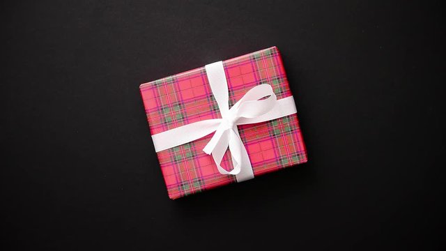 Gift box wrapped with red checkered pattern christmas paper with white bow on black table, top view