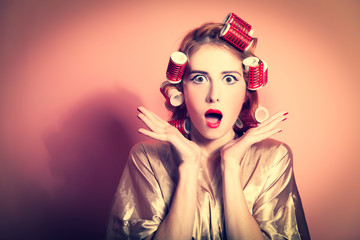 Surprised housewife with curlers on pink background