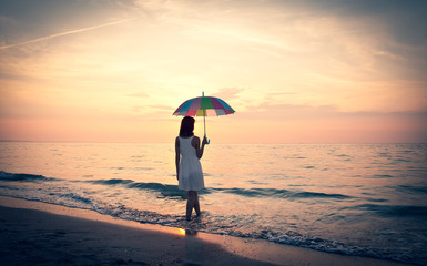 Young beautiful girl on the beach at sunrise with umbrella.