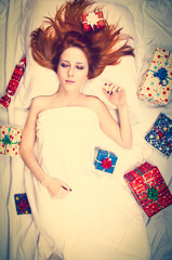 Obraz na płótnie Canvas Redhead girl in bed with gifts. Photo in warm tone style.