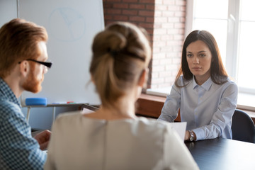 Serious attentive female boss listening to employees reporting about work results, focused applicant looking at hr at job interview, confident businesswoman thinking of difficult group negotiations