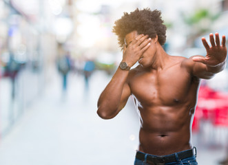 Fototapeta na wymiar Afro american shirtless man showing nude body over isolated background covering eyes with hands and doing stop gesture with sad and fear expression. Embarrassed and negative concept.