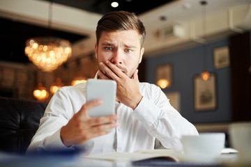 Scared young businessman reading phone