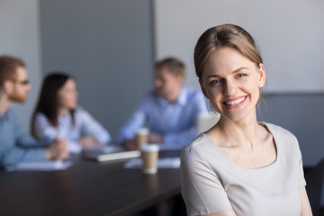 Smiling young attractive professional businesswoman looking at camera in office with colleagues at...