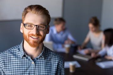 Smiling red-haired millennial business man in glasses looking at camera posing at meeting, young...