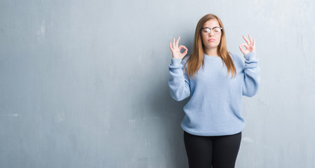 Young adult woman over grey grunge wall wearing glasses relax and smiling with eyes closed doing meditation gesture with fingers. Yoga concept.