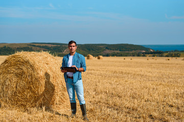 Frontal portrait of man botanist farmer with a tablet in blue jeans and a shirt and a white t-shirt in a field with haystacks