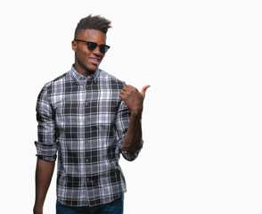 Young african american man wearing sunglasses over isolated background smiling with happy face looking and pointing to the side with thumb up.