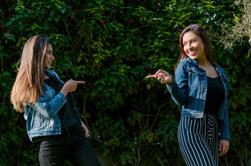 Fototapeta premium Cheerful friends are gossiping in the park. The girls are pointing with their finger and laughing.