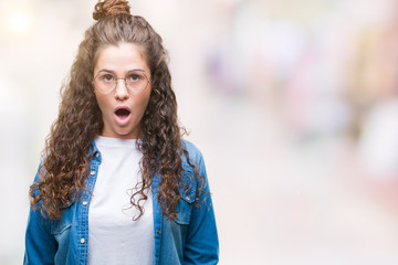 Beautiful young brunette curly hair girl wearing glasses over isolated background afraid and shocked with surprise expression, fear and excited face.