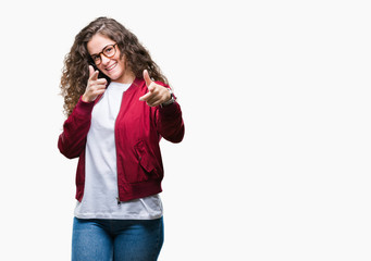 Beautiful brunette curly hair young girl wearing jacket and glasses over isolated background pointing fingers to camera with happy and funny face. Good energy and vibes.