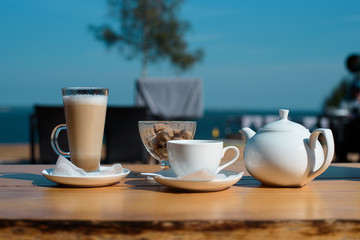 Concept of awakening. set of latte mugs, cup of tea and a teapot with cane sugar on the summer terrace