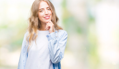 Beautiful young blonde woman over isolated background looking confident at the camera with smile with crossed arms and hand raised on chin. Thinking positive.