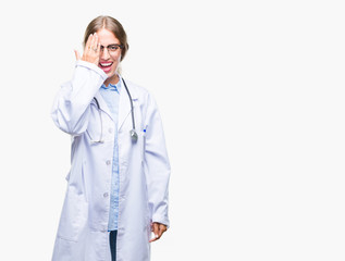 Beautiful young blonde doctor woman wearing medical uniform over isolated background covering one eye with hand with confident smile on face and surprise emotion.