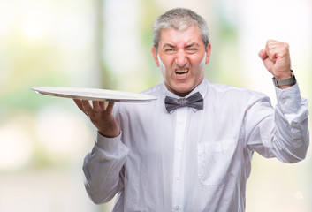 Handsome senior waiter man holding silver tray over isolated background annoyed and frustrated...