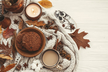 Stylish Autumn Flat Lay. Delicious coffee,cookies and beautiful fall leaves, candle, nuts, acorns, cotton, cinnamon on sweater and white rustic background top view. Cozy autumn image