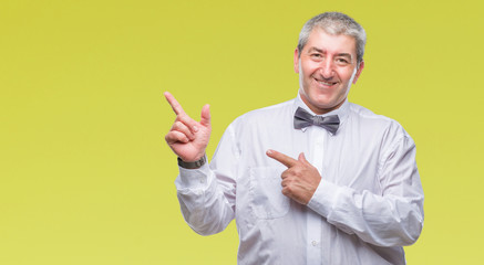 Fototapeta premium Handsome senior man wearing bow tie over isolated background smiling and looking at the camera pointing with two hands and fingers to the side.