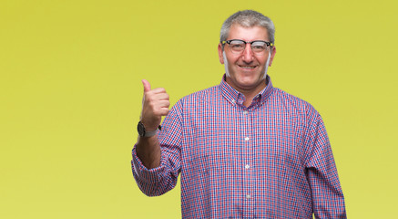Handsome senior man wearing glasses over isolated background smiling with happy face looking and pointing to the side with thumb up.