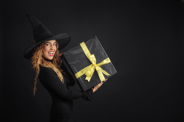 Black Friday. Halloween witch with a black hat on a black background holding gift boxes with juruse...